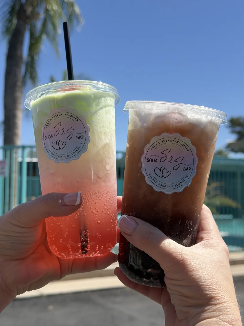 Two S2S Soda Bar drinks raised in a toast under a palm tree